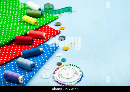 Sewing accessories and multi-colored fabrics on a blue wooden background. Fabrics, measuring tape, pins, buttons and thread. Stock Photo