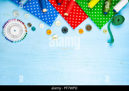 Sewing accessories and multi-colored fabrics on a blue wooden background. Fabrics, measuring tape, pins, buttons and thread. Stock Photo