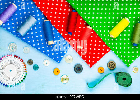 Sewing accessories and multi-colored fabrics on a blue wooden background. Fabrics, measuring tape, pins, buttons and thread. Stock Photo