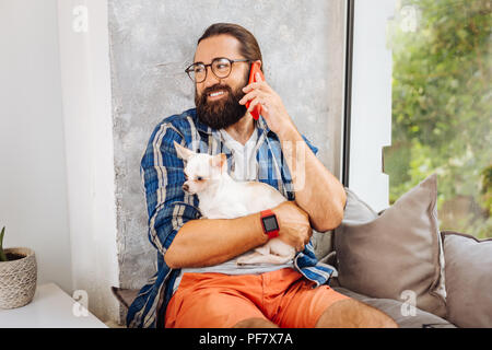 Dark-eyed smiling man calling his wife while holding little dog Stock Photo