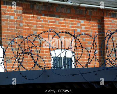 Coiled barbed wire on top of brick wall Stock Photo