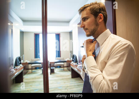 People, business,fashion and clothing concept - close up of man in shirt dressing up and adjusting tie on neck at home. Stock Photo