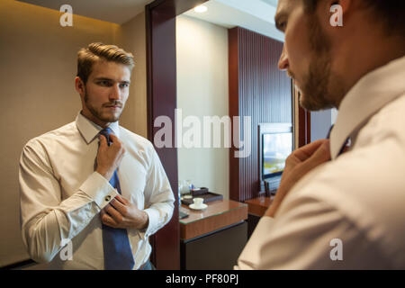 People, business,fashion and clothing concept - close up of man in shirt dressing up and adjusting tie on neck at home. Stock Photo