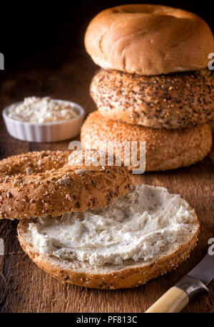 A delicious whole grain bagel with herbed cream cheese on a rustic wood table. Stock Photo