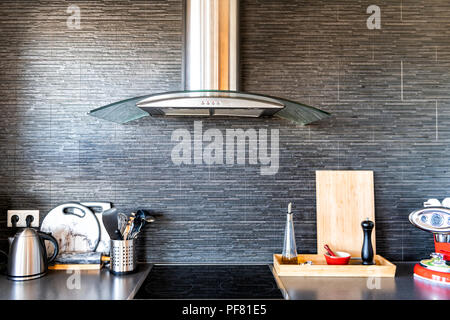 Modern, clean interior of kitchen with cooking utensils, tea pot or kettle, cutting board, coffee maker, electric stove, spices containers, stone wall Stock Photo
