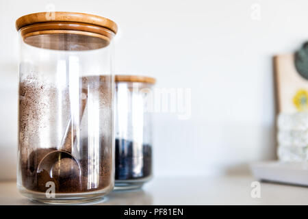 Closeup of two kitchen spices closed glass jars with wooden lids, coffee, cocoa, or cinnamon, measuring, measurement spoon inside, reflection Stock Photo