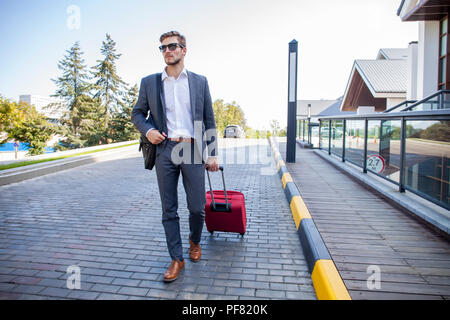 Businessman walking from hotel lobby. Full length portrait of young executive with a suitcase. Stock Photo