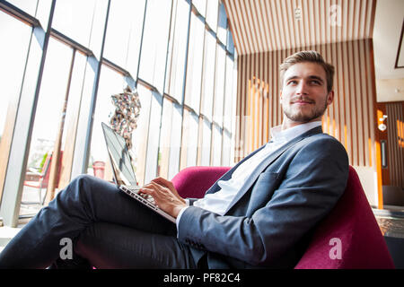 Young businessman working on laptop, sitting in hotel lobby waiting for someone. Stock Photo