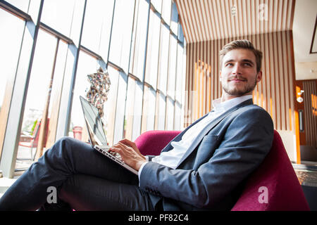 Young businessman working on laptop, sitting in hotel lobby waiting for someone.