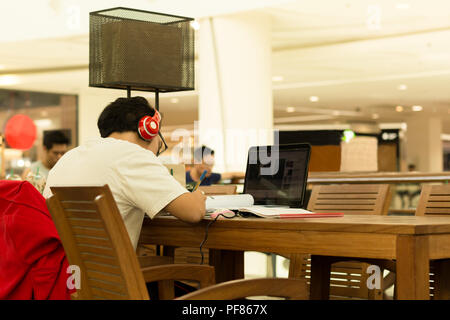 Student with headphones on doing home work in cafe with laptop on table Stock Photo