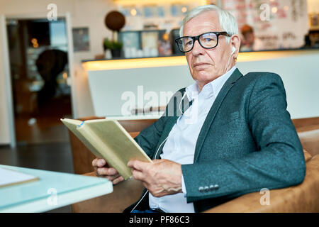 Pensive Senior Man Reading Book in Cafe Stock Photo