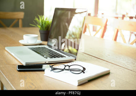 Selected focus laptop with cell phone notebook and glasses and coffee cup on wooden desk Stock Photo