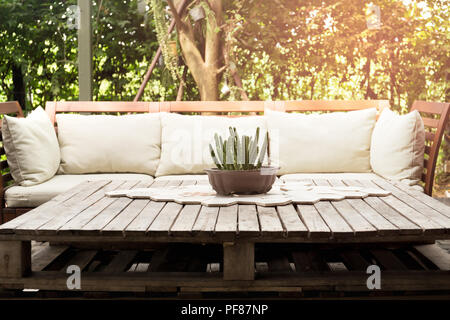 Wooden garden lounge chair with cushion and small cactus on the table in the garden with sunlight Stock Photo
