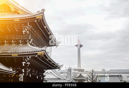 The famous heritage, traditional temple Hongan-ji with golden roof with Kyoto tower in dramatic bright morning sunrise light in Japan Stock Photo