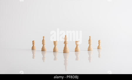 Queen chess piece with chess figures standing on white table in a conceptual image with copy space. Stock Photo