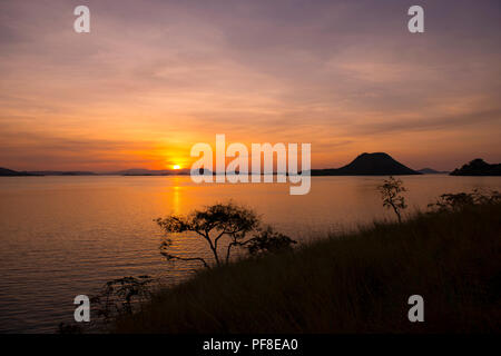 A view of the sunset over Komodo Island on the horizon, with ocean and islands in the foreground, as seen from a headland on Flores, Komodo, Indonesia Stock Photo