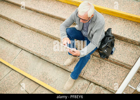 Aged businessman with tablet on stairs Stock Photo