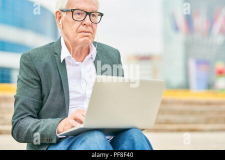 Elderly entrepreneur listening to music and using laptop Stock Photo