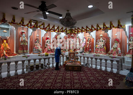 A Hindu woman prays and meditates in front of statues of deities at the Satya Narayan Mandir in Elmhurst, Queens, New York. Stock Photo