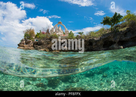 Underwater split-level photo in shallow tropical water of Buddhist temple & Ganesh statue at Menjangan Island, Bali, Indonesia, with blue sky above. Stock Photo