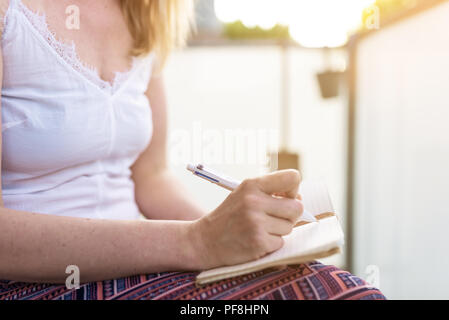 woman sitting on patio taking notes in notebook Stock Photo