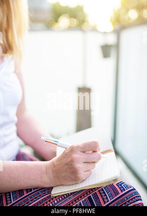 close-up of woman sitting on patio taking notes in notebook Stock Photo