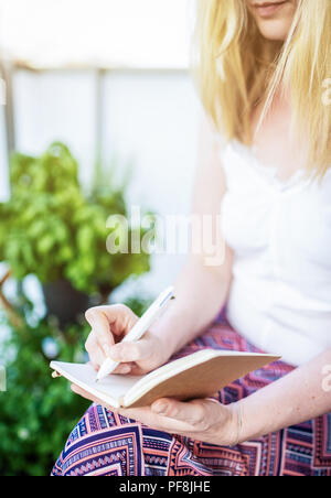 woman sitting on patio taking notes in notebook Stock Photo