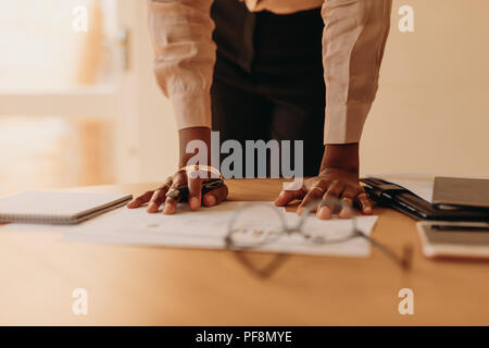 Close up of hands of a woman entrepreneur holding pen resting on the table. Businesswoman reading a document at home standing beside a table while res Stock Photo