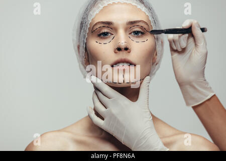 Woman in medical headwear with dotted lines drawn on her face and beautician holding scalpel for plastic surgery. Woman having anti aging and face lif Stock Photo