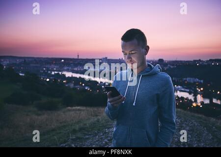 Loneliness handsome man using mobile phone against urban skyline at sunrise. Stock Photo