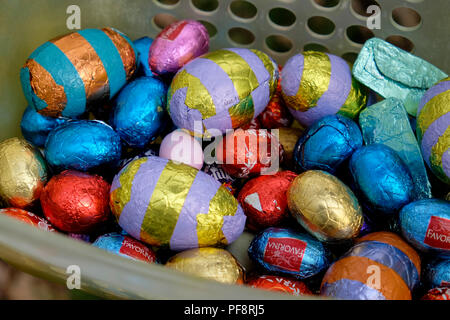 Closeup of chocolate Easter eggs wrapped in colourful foil from various stores in a basket collected by a child on an Easter egg hunt UK  KATHY DEWITT Stock Photo