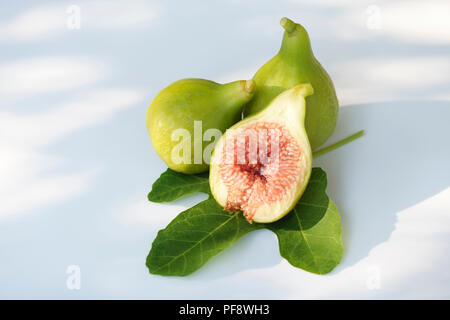 Freshly picked, ripe, organic Kadota figs on a fig leaf, with one fruit sliced in half showing red pulp, artistic food still life isolated on white ba Stock Photo