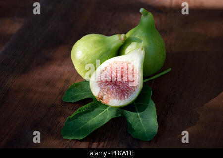 Organically grown freshly picked ripe Kadota figs on a fig leaf, with one fruit sliced in half, artistic food still life on wood background Stock Photo