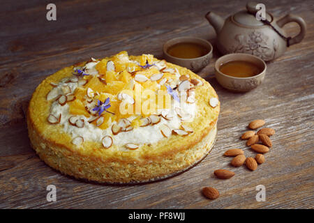 Healthy home-made flourless, sugar-free, dairy-free vegan cake made of almond flour, oranges and coconut, artistic food still life with a clay teapot  Stock Photo
