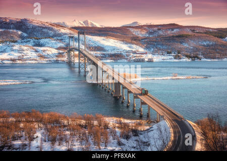 Beautiful bridge during sunset in Lofoten islands, Norway. Aerial winter landscape with cars on the road, blue sea, trees, snowy mountains, colorful r Stock Photo