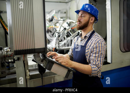 Side view portrait of machine operator wearing hardhat standing at control panel pressing buttons, copy space Stock Photo