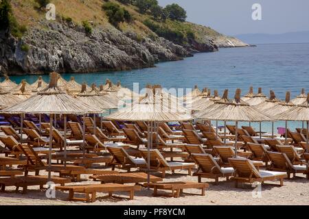 deserted beach couches and straw parasols ready for customers on a summer day on the adriatic coast of Albania Stock Photo