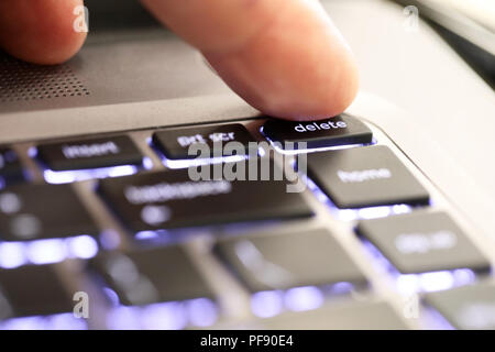 close up of a finger hitting pushing the delete symbol button tab on an illuminated laptop computer key board. The delete key Stock Photo