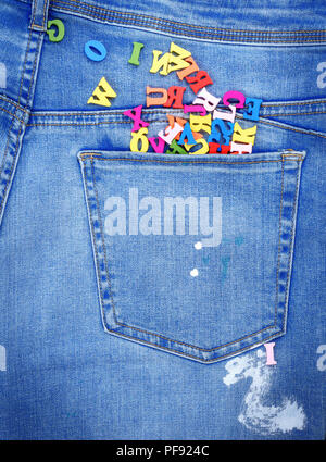 multicolored wooden letters of the English alphabet pour out from the back pocket of the jeans, close up Stock Photo