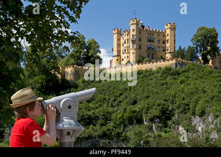 boy looking through a telescope in front of Hohenschwangau Castle, Hohenschwangau, Allgaeu, Bavaria, Germany Stock Photo