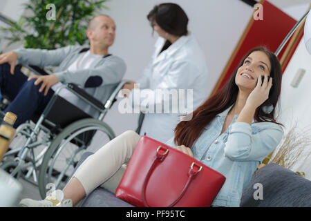 woman in clinic waiting room speaking at phone smiling Stock Photo