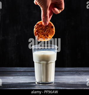 A hand dunking a cookie in a glass of milk over a black background Stock Photo