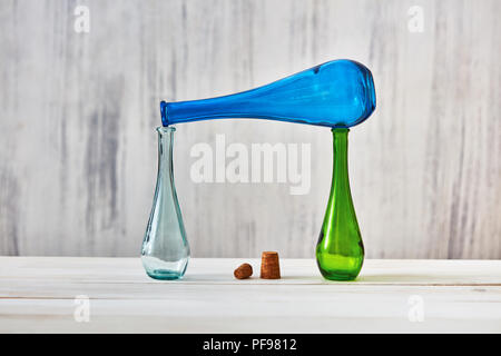 Two glass bottles stand on a table, a blue bottle lies on top of them with with corks on a light gray background. Concept of saving homemade products. Stock Photo