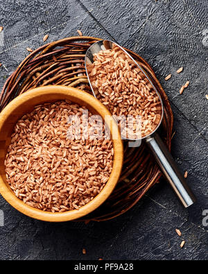 Wild brown rice in wooden bowl on black background. Top view of grains. Stock Photo