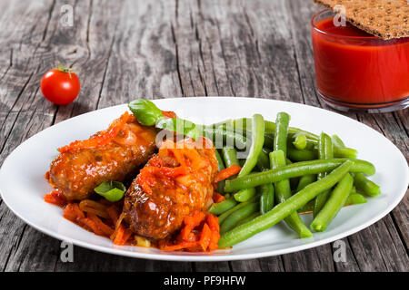 Delicious Meat Cutlets stewed with onion, carrot tomato sauce, decorated with basil leaves on a white dish with boiled green bean, glass with tomato j Stock Photo