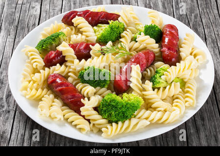 Delicious Spiral Pasta salad with  broccoli and grilled sausages decorated with dill on a white dish on an rustic table, studio lights, close-up Stock Photo