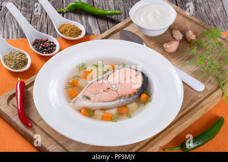 Hearty salmon soup on a white plate with spices, hot pepper and cream sauce, served on an orange table napkin at the rustic wooden table close-up Stock Photo