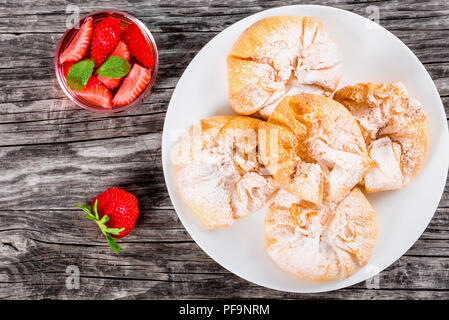 coconut and strawberry puff pastries on a white dish on an old wooden background with strawberry mint cold soft drink, view from above Stock Photo