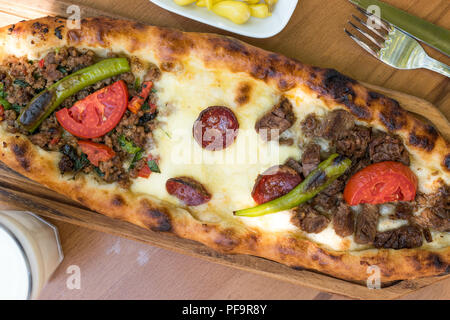 Turkish Mixed Pide with Minced Meat, Cheese, Sausage (Sucuk), Tomatoes and Red Pepper served with Salad and Pickles. Traditional Food.