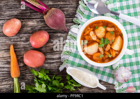 beans, new potatoes, beets, carrots, onions, tomato soup in a white mug on a checkered napkin with a spoon. ingredients on old wooden table top, view  Stock Photo